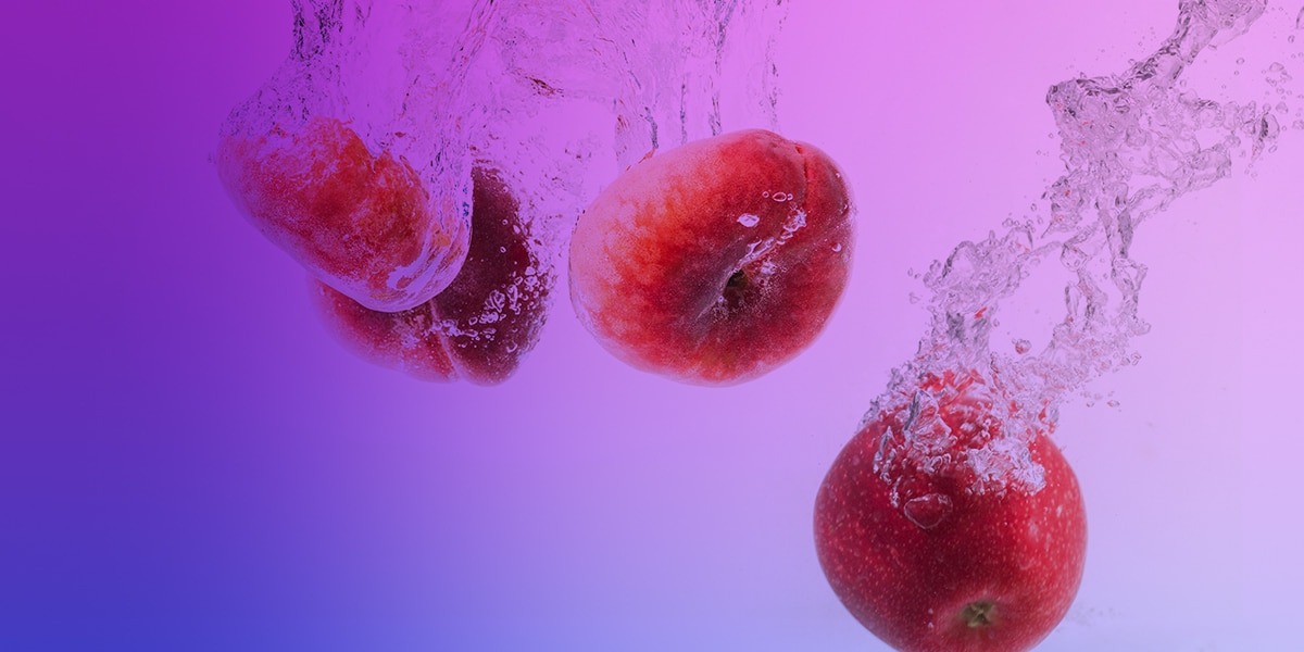 Stimmungsbild mit Pfirsichen und einem Apfel im Wassersplash vor lila Hintergrund, 20 mg