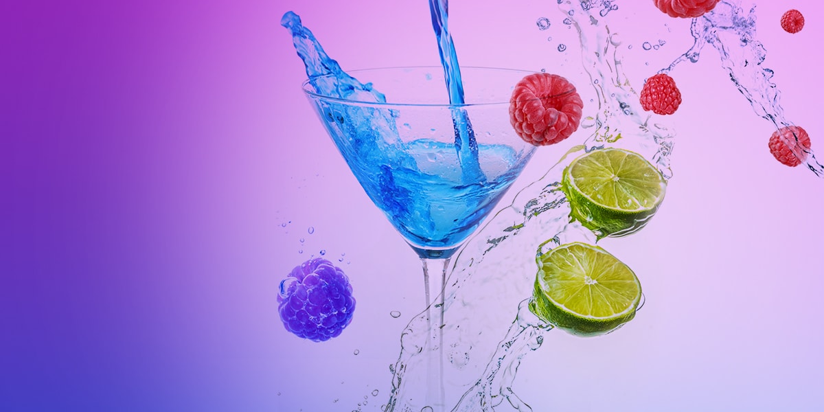 Blauer Drink im Cocktailglas mit Wasserspritzern, Himbeeren und Limettenscheiben auf violettem Hintergrund, 20 mg