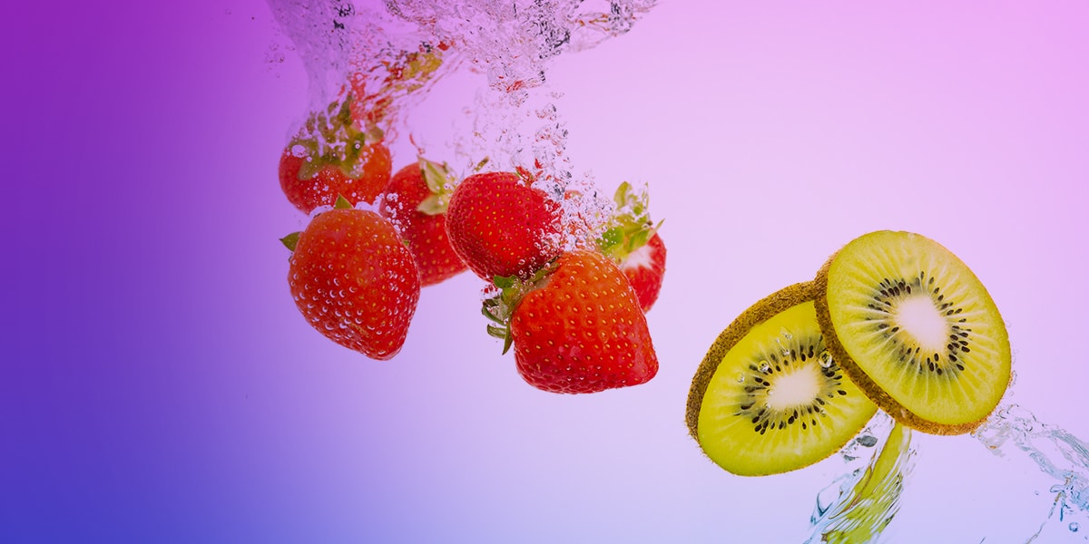 Motivbild mit Erdbeeren und aufgeschnittener Kiwi im Wassersplash vor lila Hintergrund